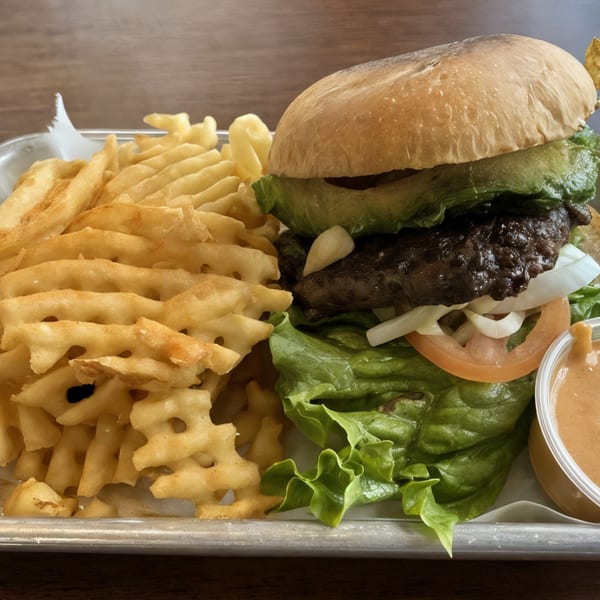 Bull Chicks burger with avocado, lettuce, tomato, onion, and a side of waffle fries with dipping sauce.