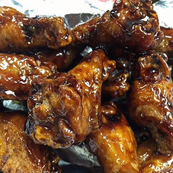 Close-up of Bull Chicks' glistening, saucy chicken wings, piled high in a foil container.