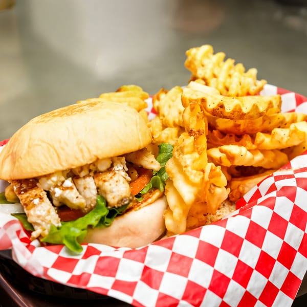Bull Chicks chicken burger with lettuce, tomato, and waffle fries in a red and white checkered basket.