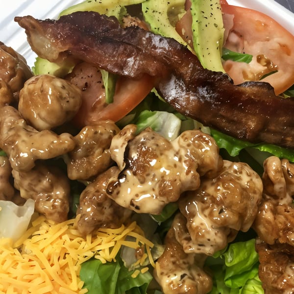 A Bull Chicks salad with crispy chicken, bacon, avocado, tomatoes, shredded cheese, and dressing.